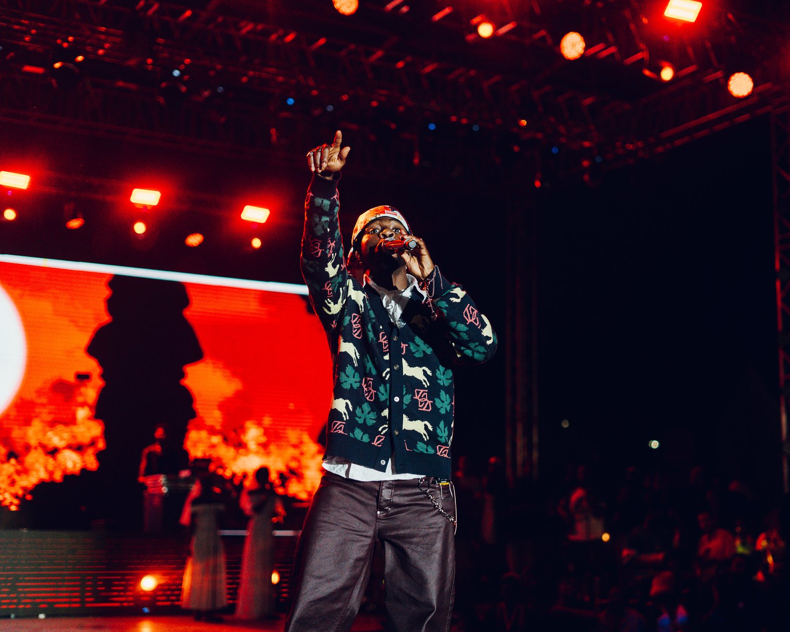 A performer in a beanie singing under stage lights
